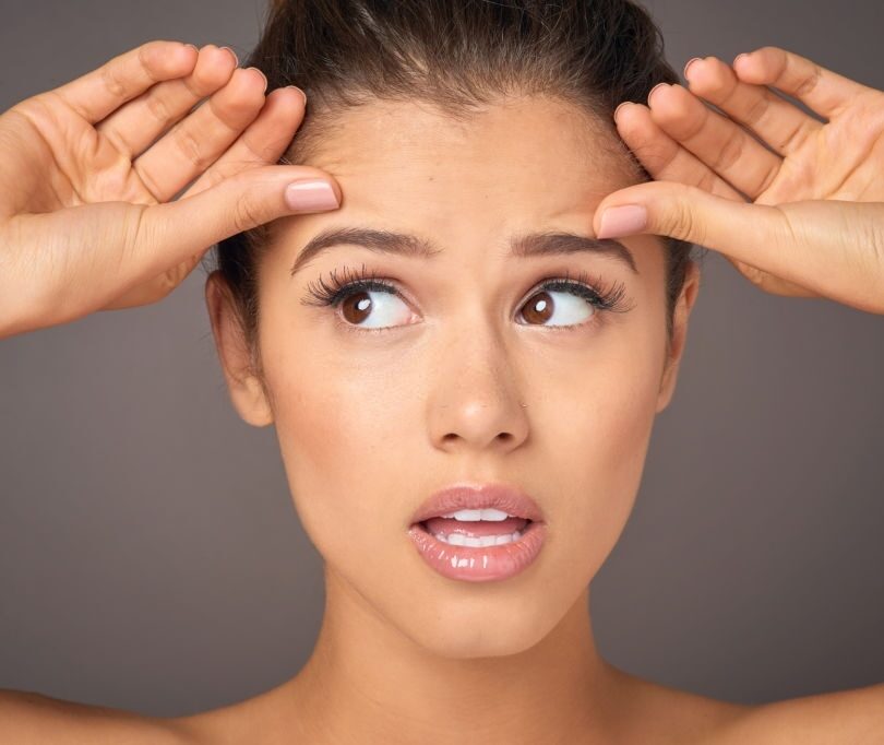 A woman with a surprised expression holding her hands up to her head.
