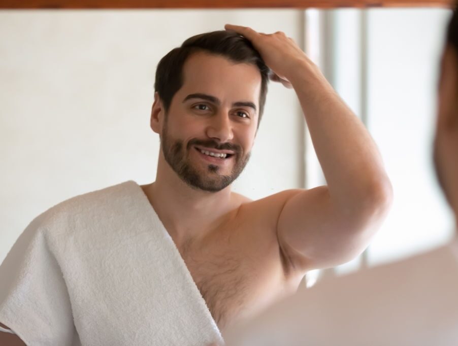 A man looking in the mirror admiring his hair restoration.