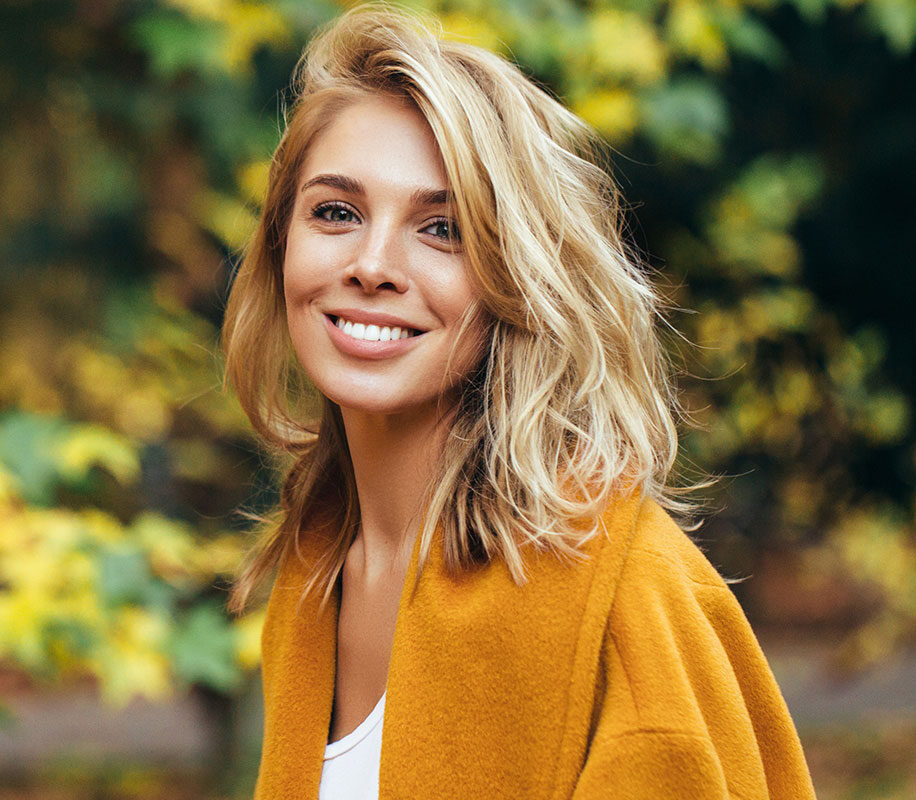 A woman smiling at the camera with trees in the background.