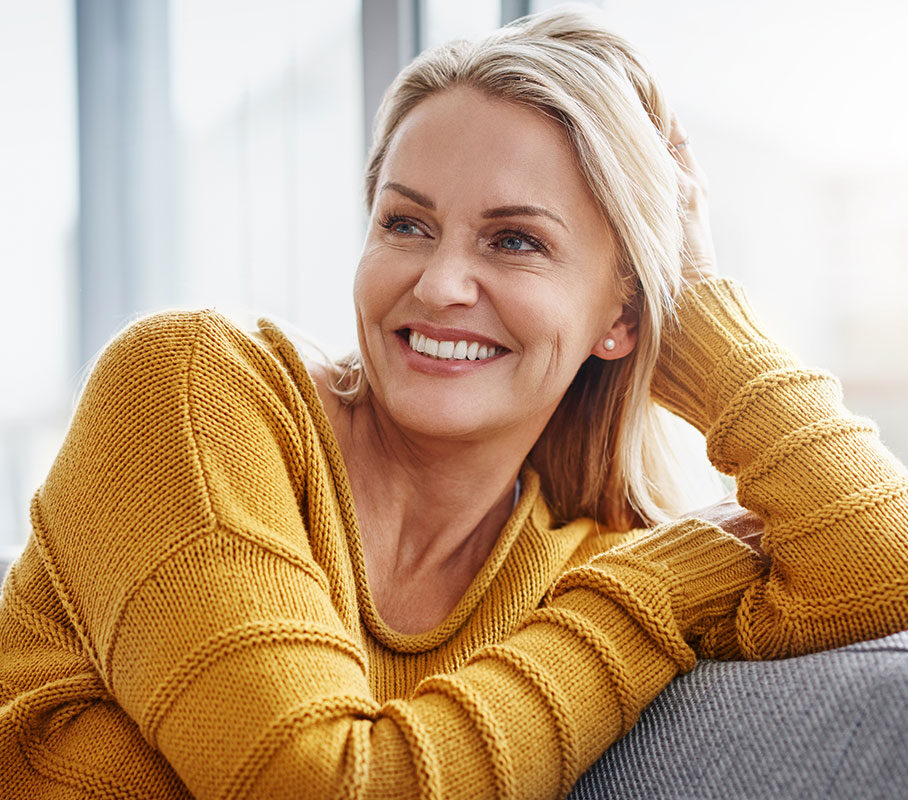 A blonde woman sitting on a couch smiling.