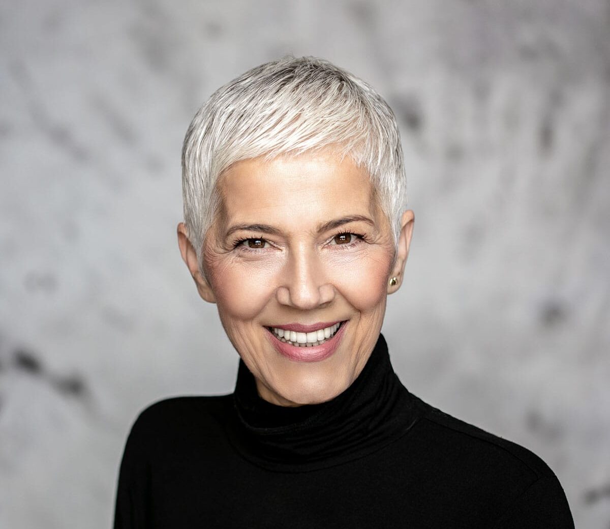 A woman with grey hair and natural makeup smiling.