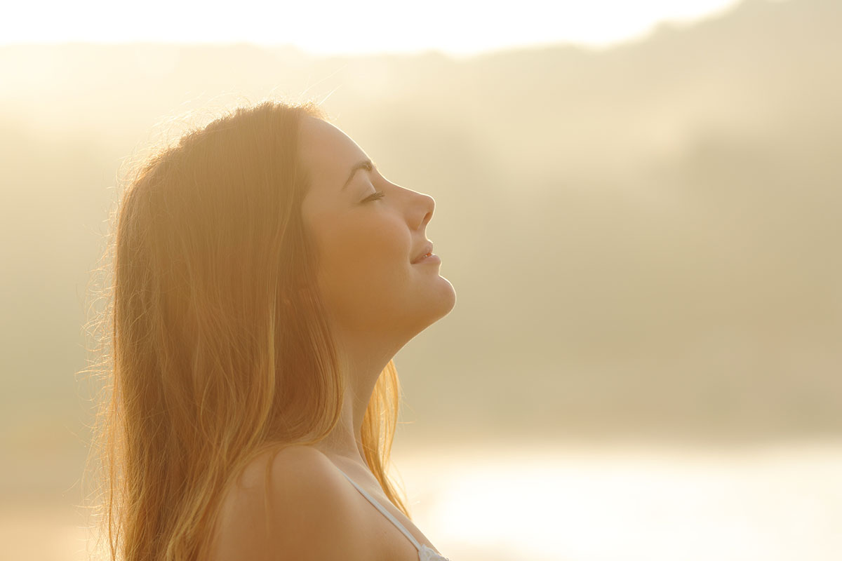 A side profile of a woman looking up at the sky with a mountain range and lake behind her.