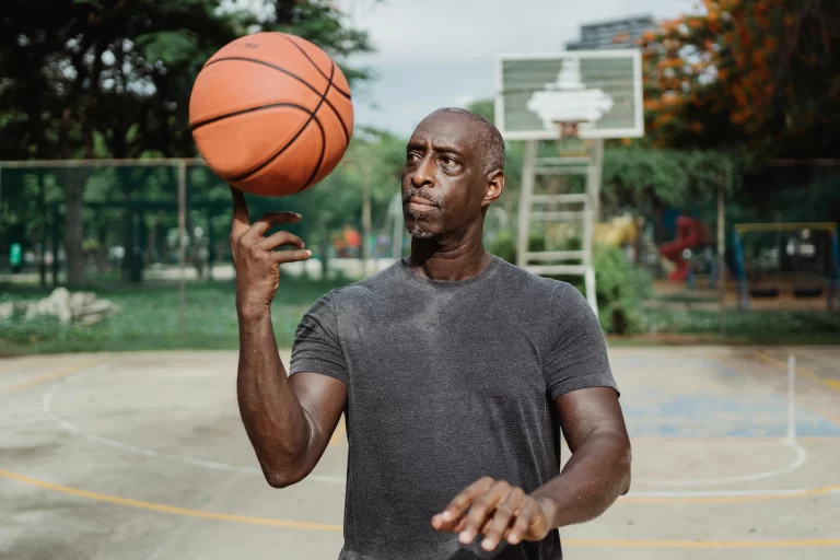 A bald man spinning a basketball on his finger on an outdoor basketball court.