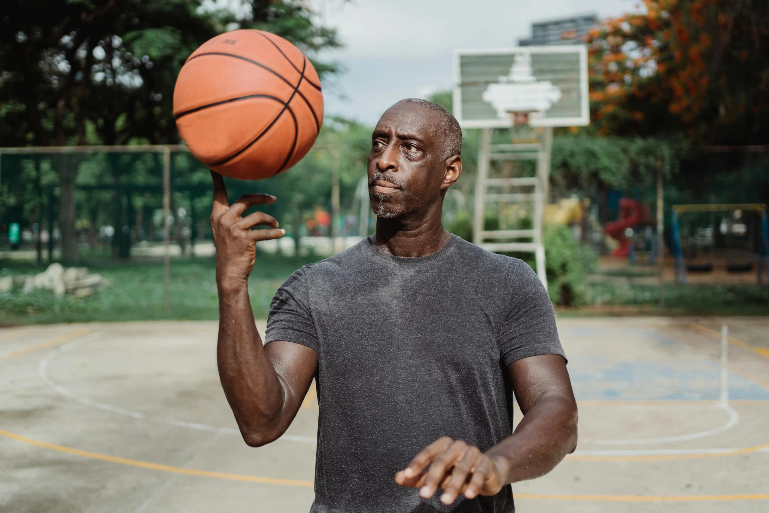 A bald man spinning a basketball on his finger on an outdoor basketball court.