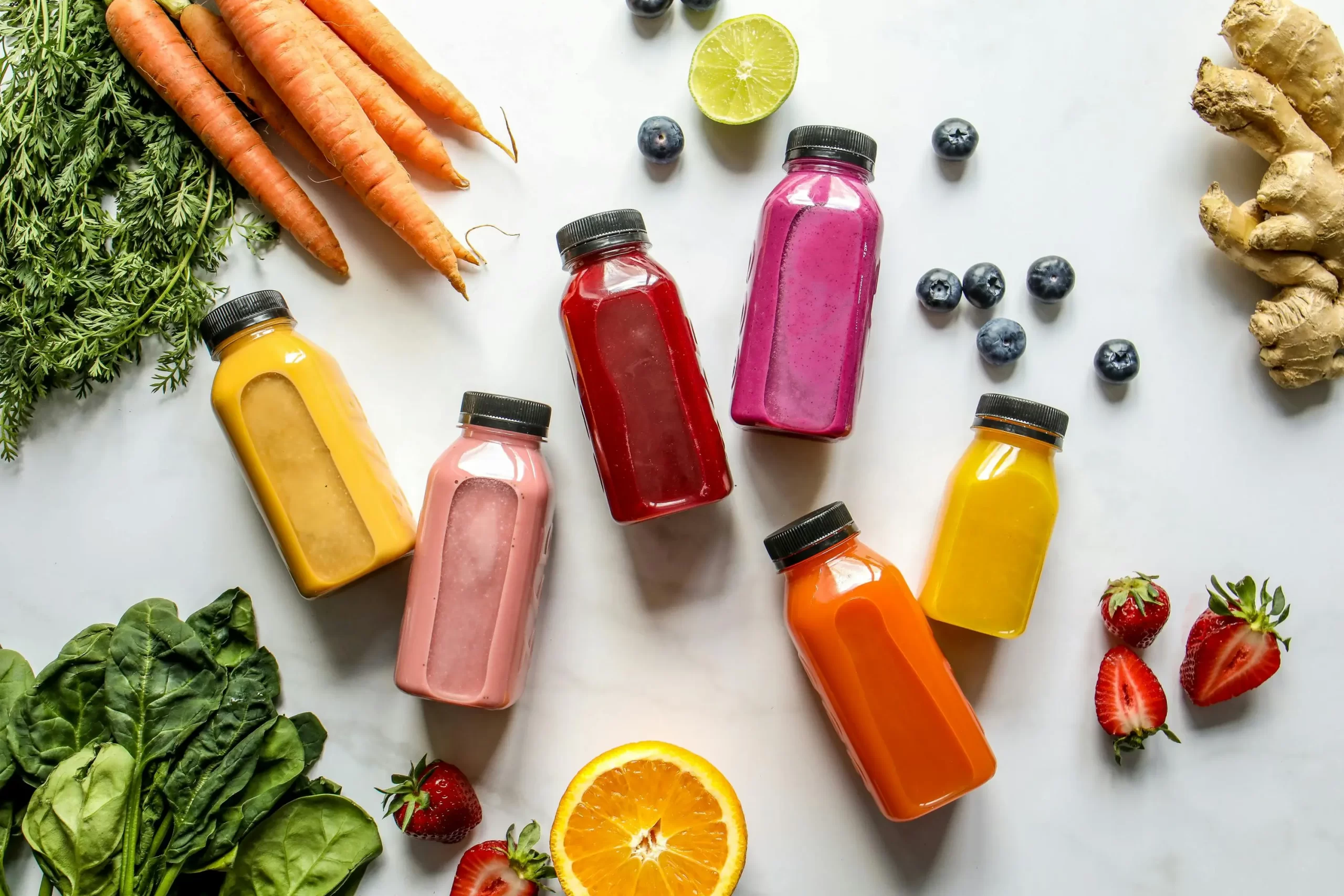 Many fruit and vegetable juices surrounded by things like carrots, oranges, kiwis, and berries.