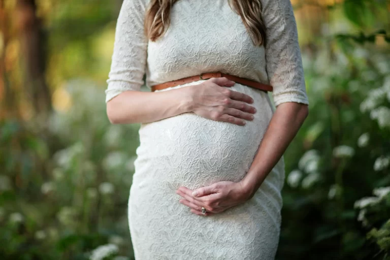 A pregnant woman holding her belly wearing a dress.