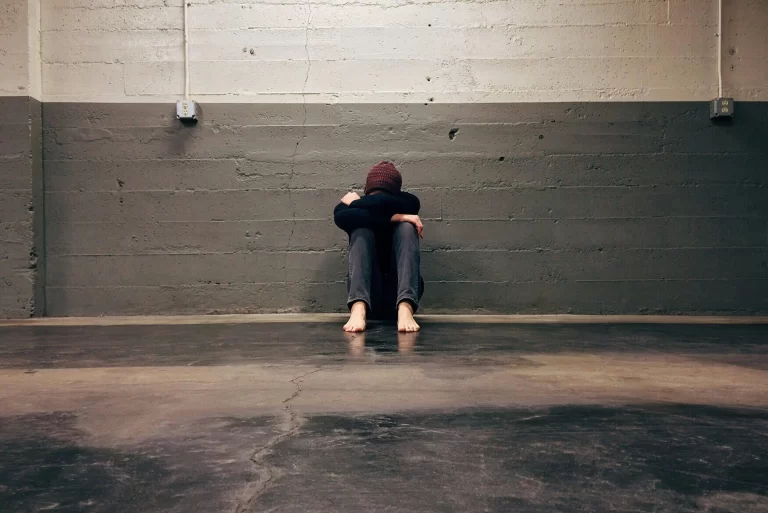 A person sitting with their head down against a wall.