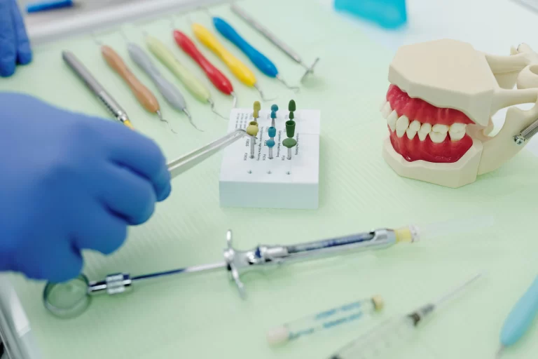 A table with a jaw model and syringes, with a medically gloved hand hovering above.