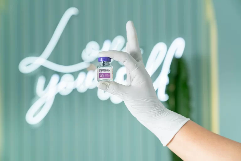 A medically-gloved hand holding a vial of Botox.
