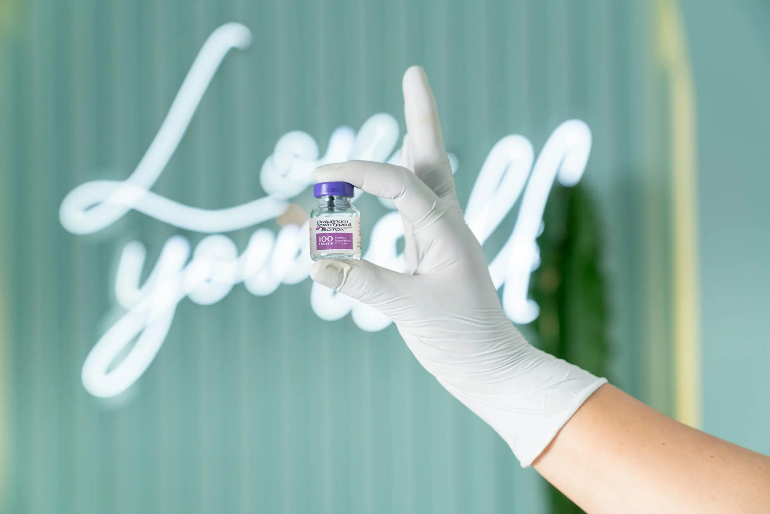 A medically-gloved hand holding a vial of Botox.