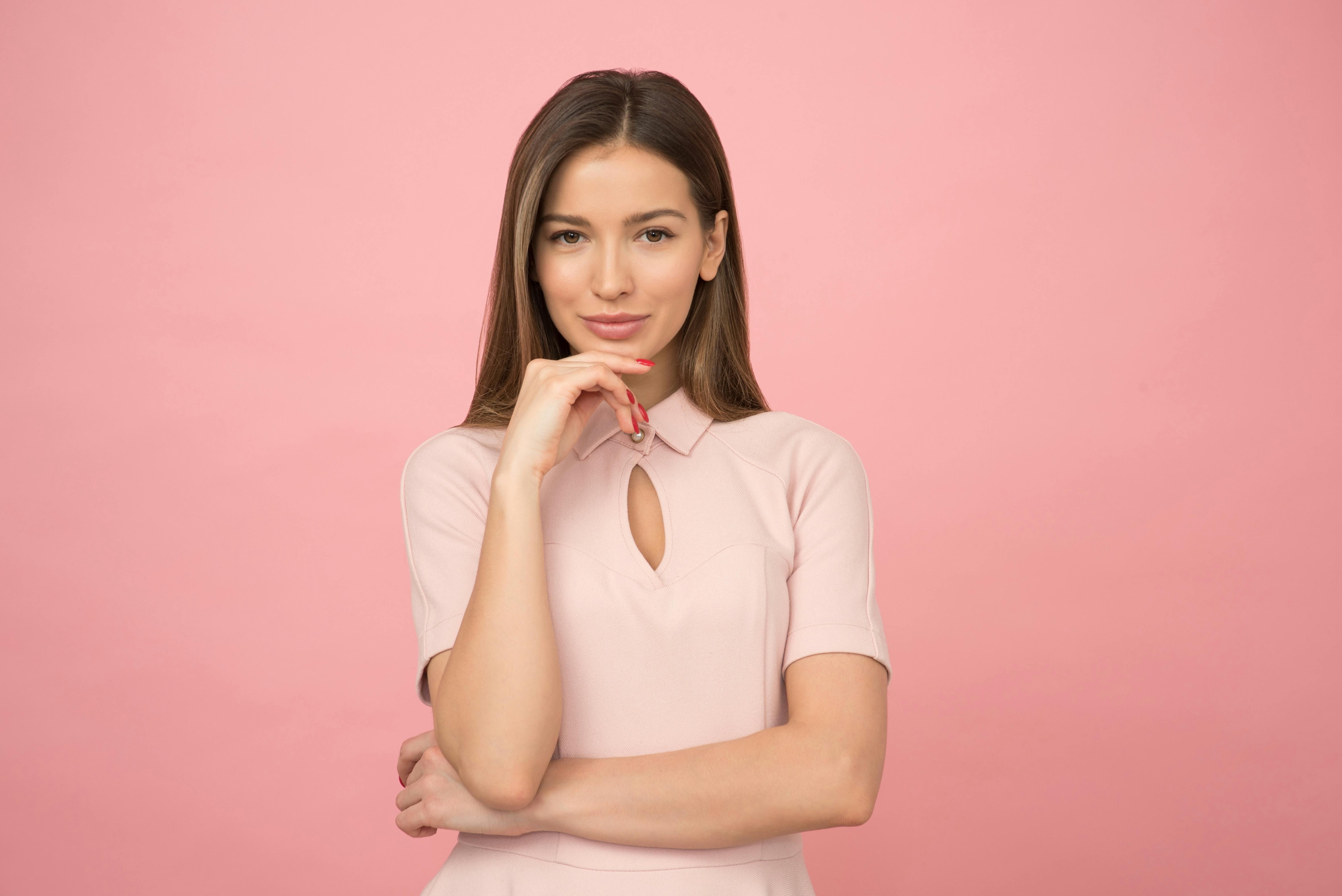 A woman with smooth facial features smiling against a pink background.