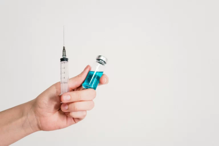 A hand holding a syringe and vial of medication.